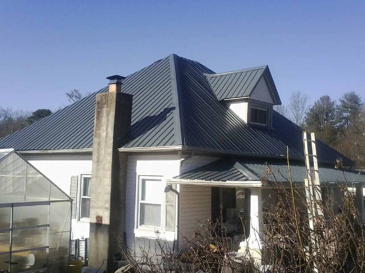 Dark blue standing seam metal roof on a white farmhouse with dormer — Slate & Tile Roof Repair by Roofing Brothers in Luray