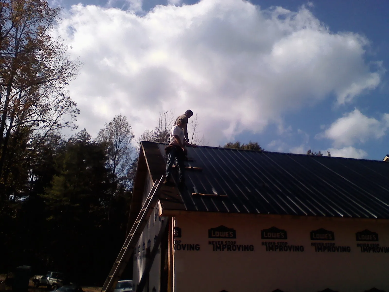 Roofer fastening dark metal panels high against a cloudy sky, from a Roof Inspection job in Luray
